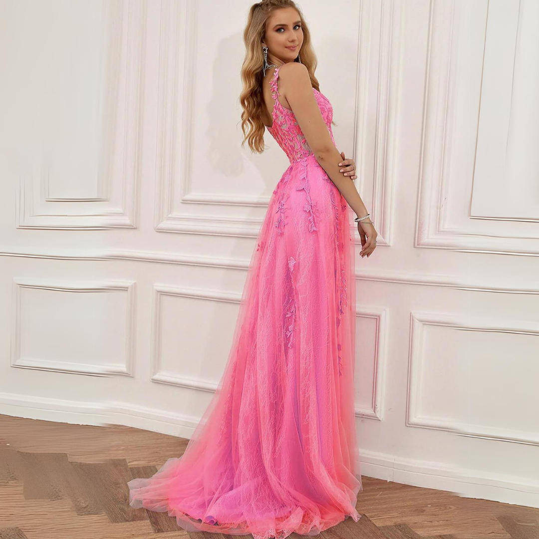 Frau in elegantem, langem, rosa Abendkleid mit Spitzenverzierungen, steht vor weißer Wand. Perfekt für Ball, Gala oder Hochzeit.