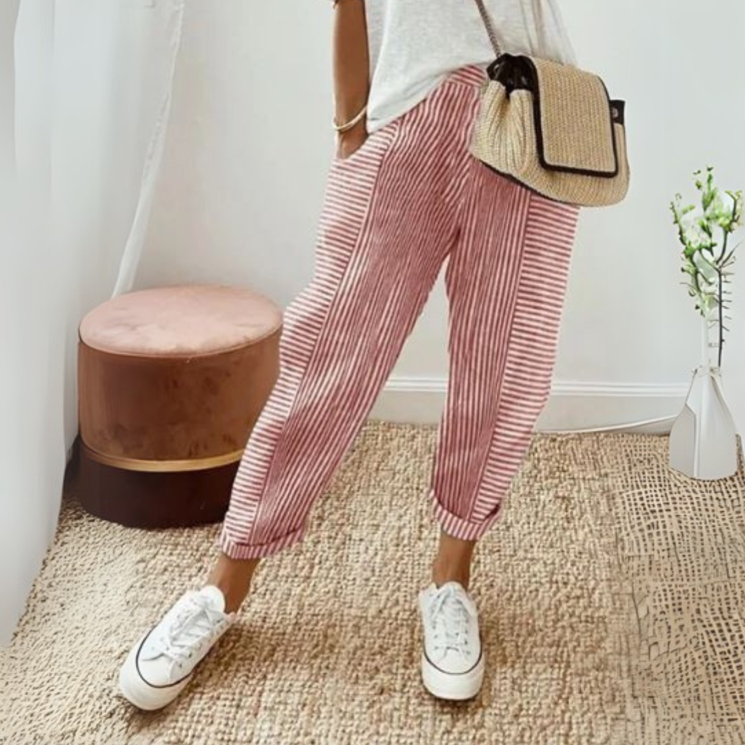 Dame in gestreifter Hose und weißen Sneakers, trägt eine Strohtasche. Moderner, lässiger Look, ideal für Sommermode und Freizeitkleidung.