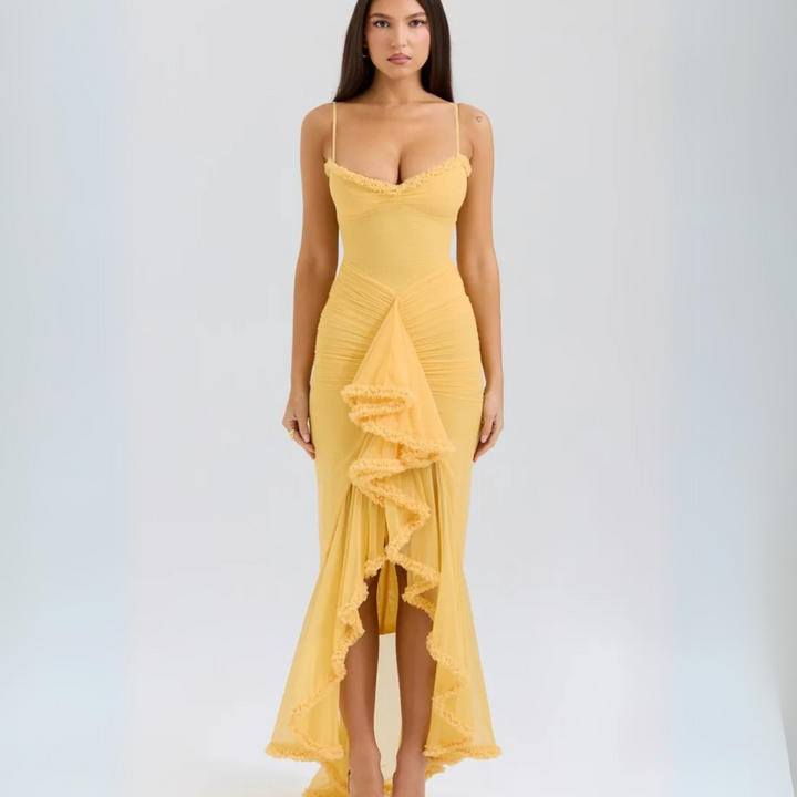 Frau in gelbem, figurbetontem Abendkleid mit Rüschen, Spaghettiträgern und asymmetrischem Saum, vor neutralem Hintergrund. Elegante Mode.