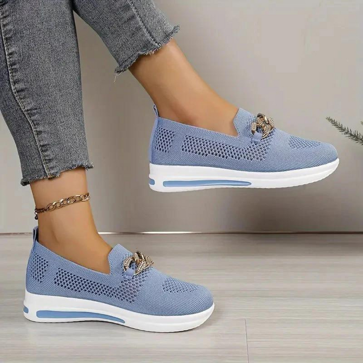 Blaue Damen-Sneaker mit weißer Sohle, atmungsaktivem Mesh-Design und dekorativer Schleife, getragen mit grauen Jeans. Modische Freizeitschuhe.