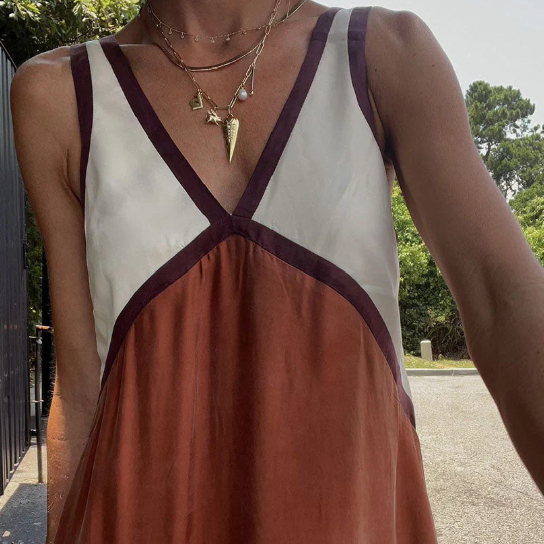 Frau in ärmellosem, dreifarbigen Kleid mit V-Ausschnitt, trägt goldene Halsketten; Sommermode, elegantes Design, Outdoor-Hintergrund.