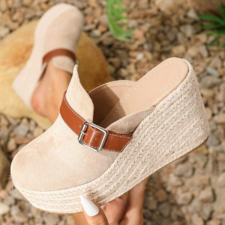 Beige Damen-Wedges mit Plateau, aus Wildleder, braunem Riemen und Schnalle, auf Kieselsteinen präsentiert. Modische Sommerschuhe.
