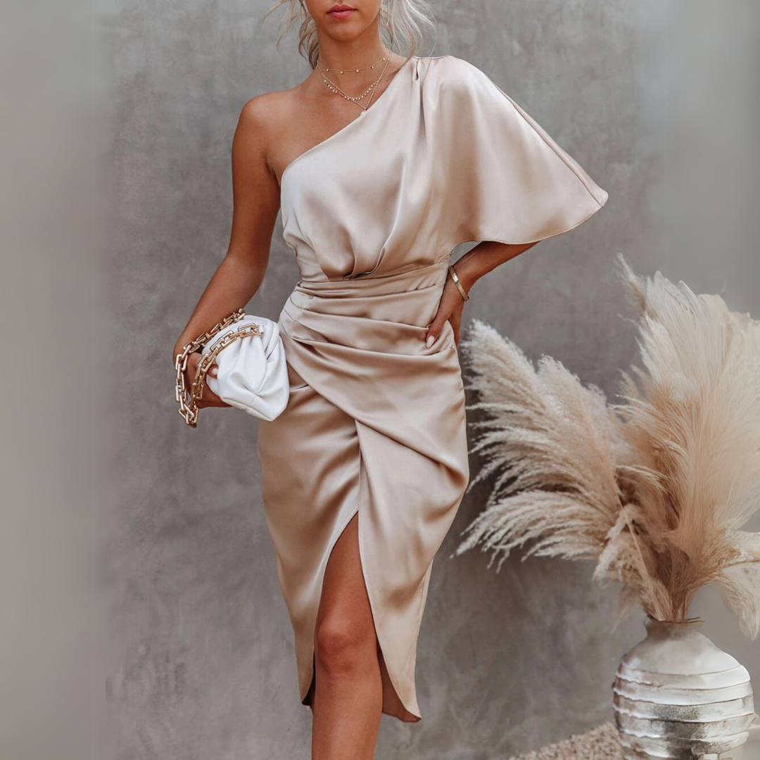 Elegantes, einseitiges Satinkleid in Champagnerfarbe, kombiniert mit weißer Clutch und Pampasgras-Dekoration im Hintergrund. Perfekt für Abendmode.