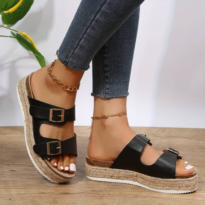 Frau trägt schwarze Plateau-Sandalen mit Schnallen und Jeans, Fußkettchen, weiße Pediküre, Sommermode, Nahaufnahme, stilvoller Look.