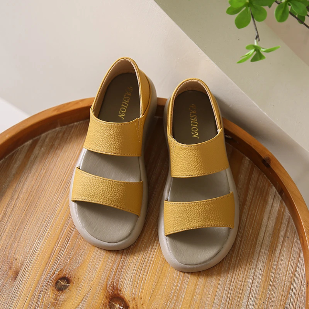 Gelbe Kindersandalen aus Leder auf einem Holztisch, modisches Design, ideal für Sommer, bequeme Passform, rutschfeste Sohle, trendige Kinderschuhe.
