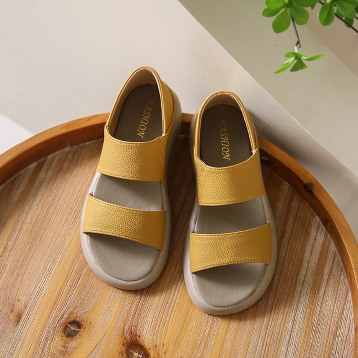 Gelbe Kindersandalen aus Leder auf einem Holztisch, modisches Design, ideal für Sommer, bequeme Passform, rutschfeste Sohle, trendige Kinderschuhe.