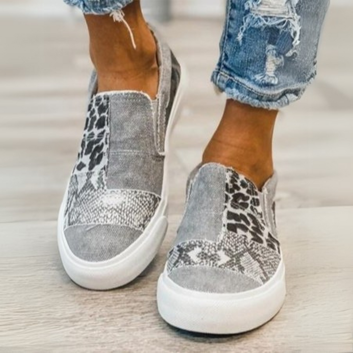 Graue Slip-On-Sneaker mit Leoparden- und Schlangenprint, getragen von Person in zerrissenen Jeans. Modische Freizeitschuhe, trendiger Animal-Print.