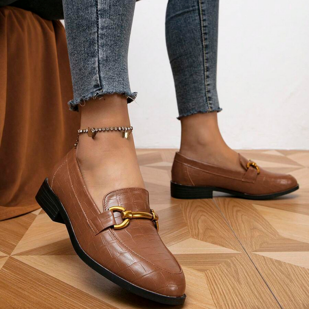 Braune Loafer mit goldener Schnalle, getragen von Person in blauen Jeans. Modische Damen-Schuhe, elegantes Design, ideal für Freizeit und Büro.