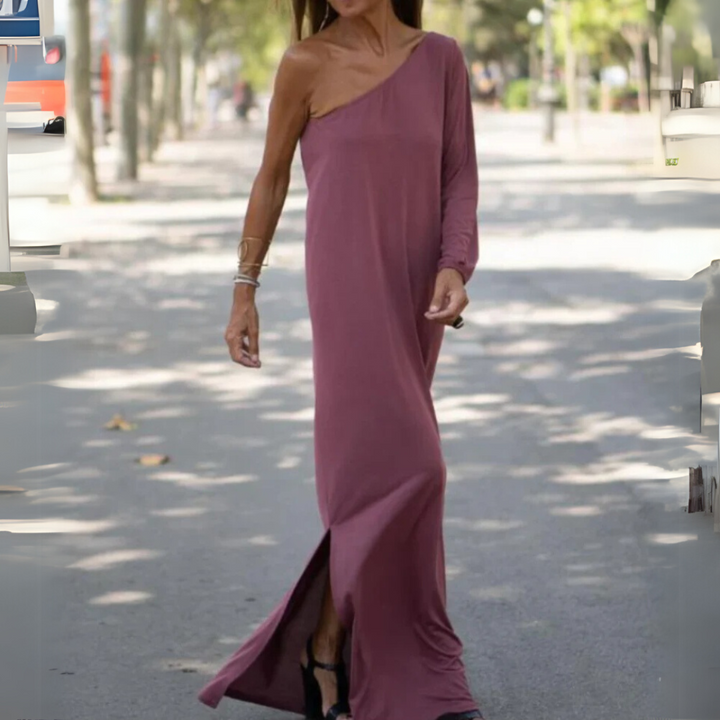 Frau in einem eleganten, einärmeligen, bodenlangen, lila Kleid spaziert auf einer sonnigen Straße. Modetrend, Sommerkleid, Streetstyle.