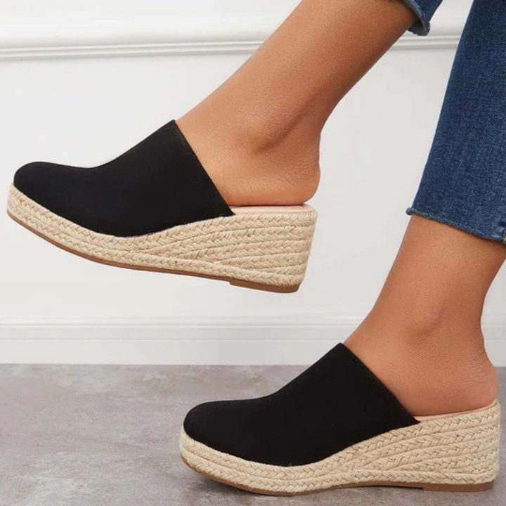 Schwarze Espadrille-Pantoletten mit Keilabsatz, geflochtener Sohle und Jeans kombiniert. Modische Damen-Sommerschuhe, bequem und stilvoll.