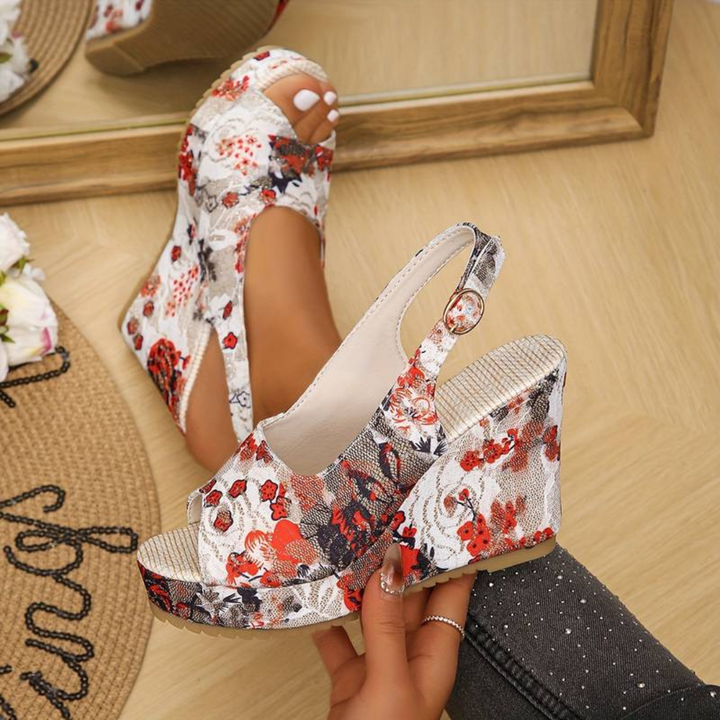 Frau trägt florale Keilsandalen mit Plateauabsatz vor einem Spiegel. Modische Sommerschuhe, Blumenmuster, elegantes Design, trendige Damenmode.