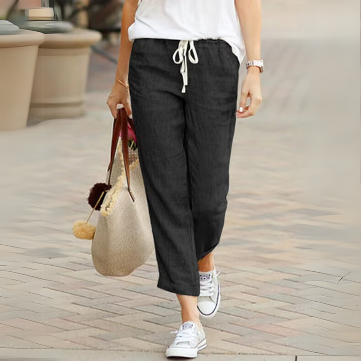 Frau in schwarzer Leinenhose und weißen Sneakers, trägt eine beige Tasche. Sommermode, lässiger Stil, bequeme Damenbekleidung.