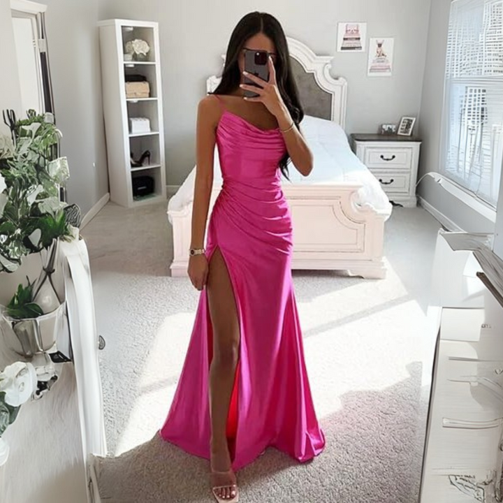 Frau in pinkem Abendkleid mit hohem Beinschlitz steht in elegantem Schlafzimmer. Modernes Interieur, Tageslicht, stilvolle Einrichtung.