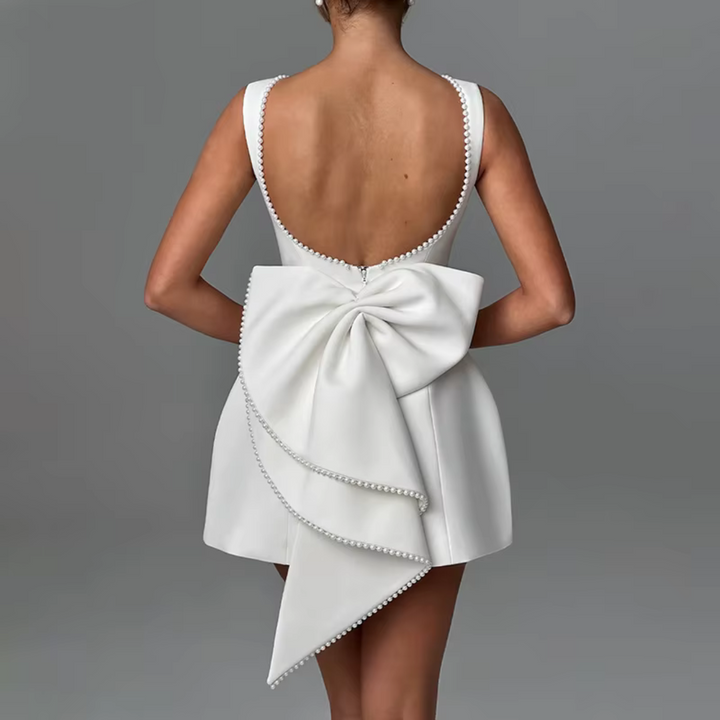 Rückenansicht eines eleganten weißen Kleides mit großem Schleifendetail und Perlenverzierung, ideal für Hochzeiten oder formelle Anlässe.