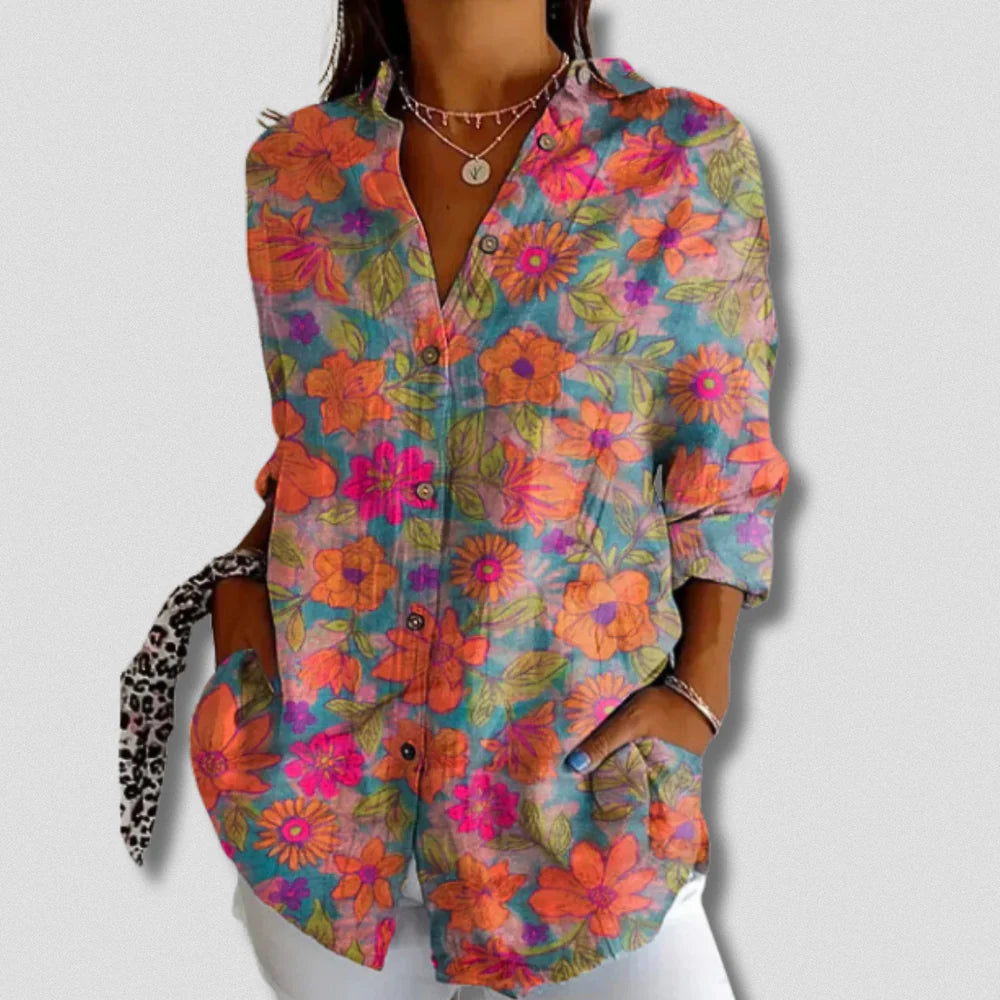 Frau trägt bunte, florale Bluse mit langen Ärmeln und Knopfleiste, kombiniert mit weißer Hose. Modetrend, Damenmode, Frühlingsoutfit.