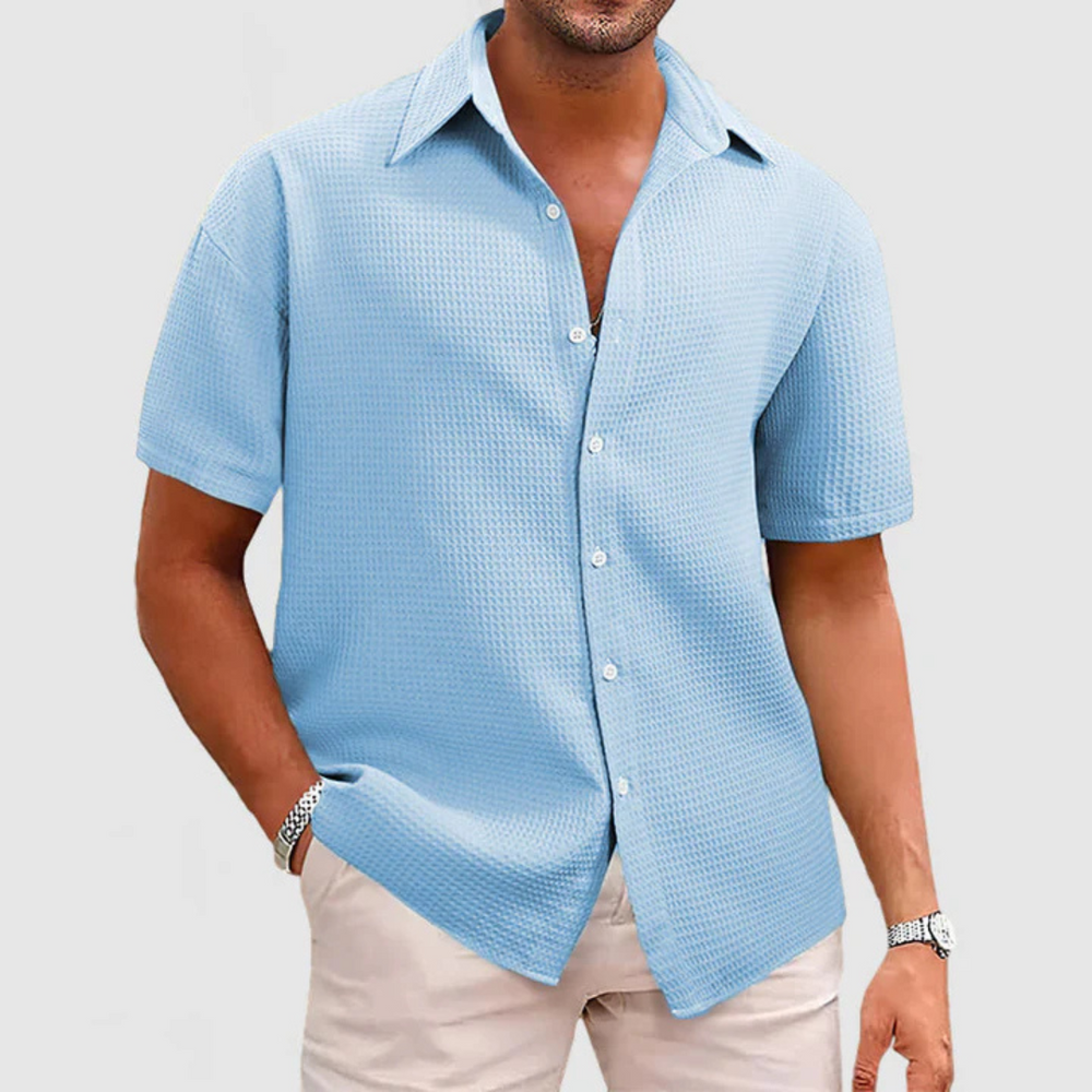 Mann in hellblauem Kurzarmhemd aus Waffelstoff, lässig offen getragen, kombiniert mit beiger Hose. Ideal für Sommermode und Freizeitlook.