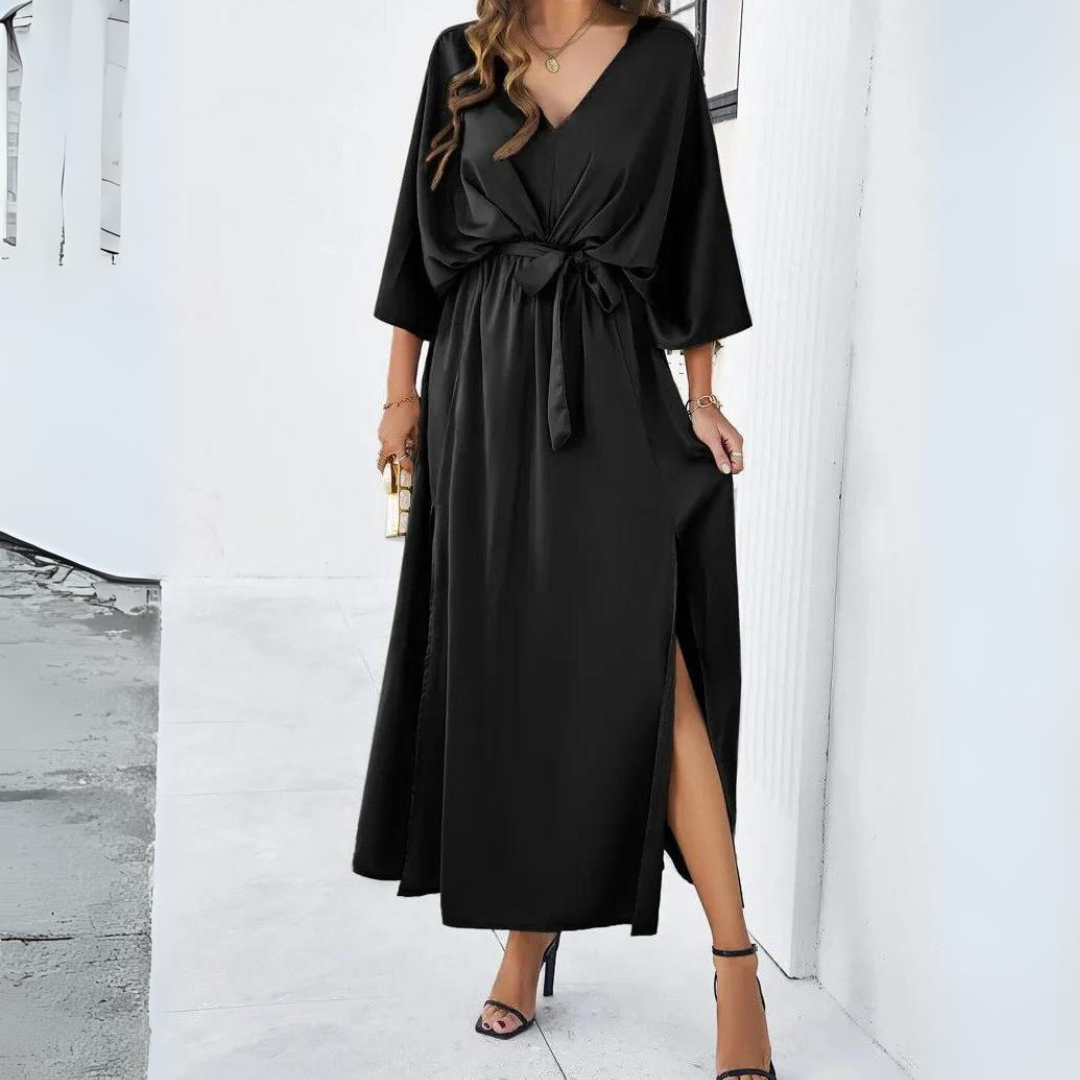 Frau in elegantem, schwarzem Maxikleid mit V-Ausschnitt und Taillengürtel, trägt High Heels. Perfekt für Abendmode und festliche Anlässe.