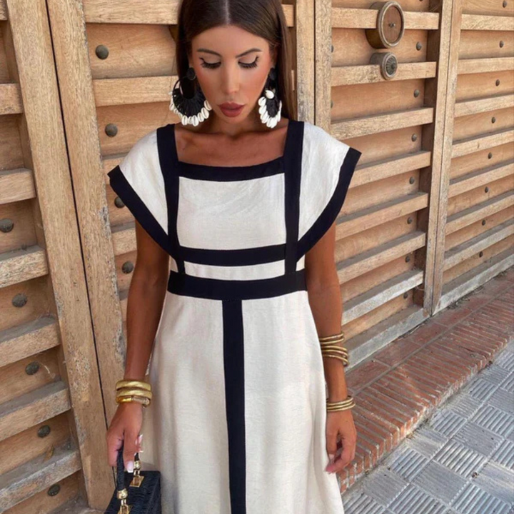 Frau in elegantem, weißem Kleid mit schwarzen Streifen, großen Ohrringen und Armreifen vor Holzwand. Sommermode, Damenkleidung, Accessoires.