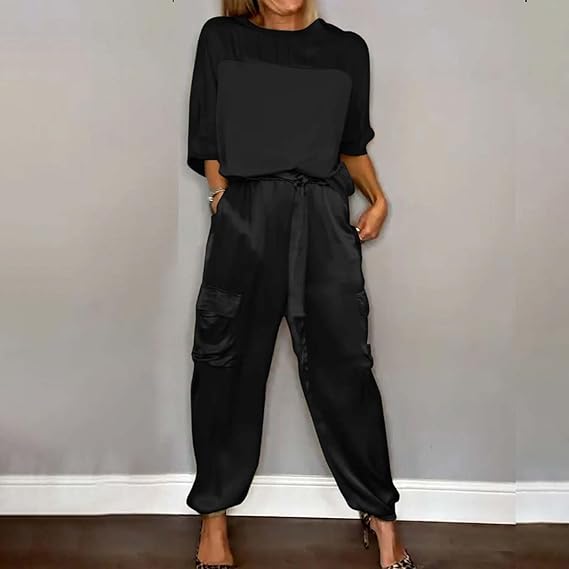 Frau in schwarzem Jumpsuit mit Taschen, lässiger Stil, steht vor grauer Wand. Modetrend, Damenbekleidung, bequemes Outfit.