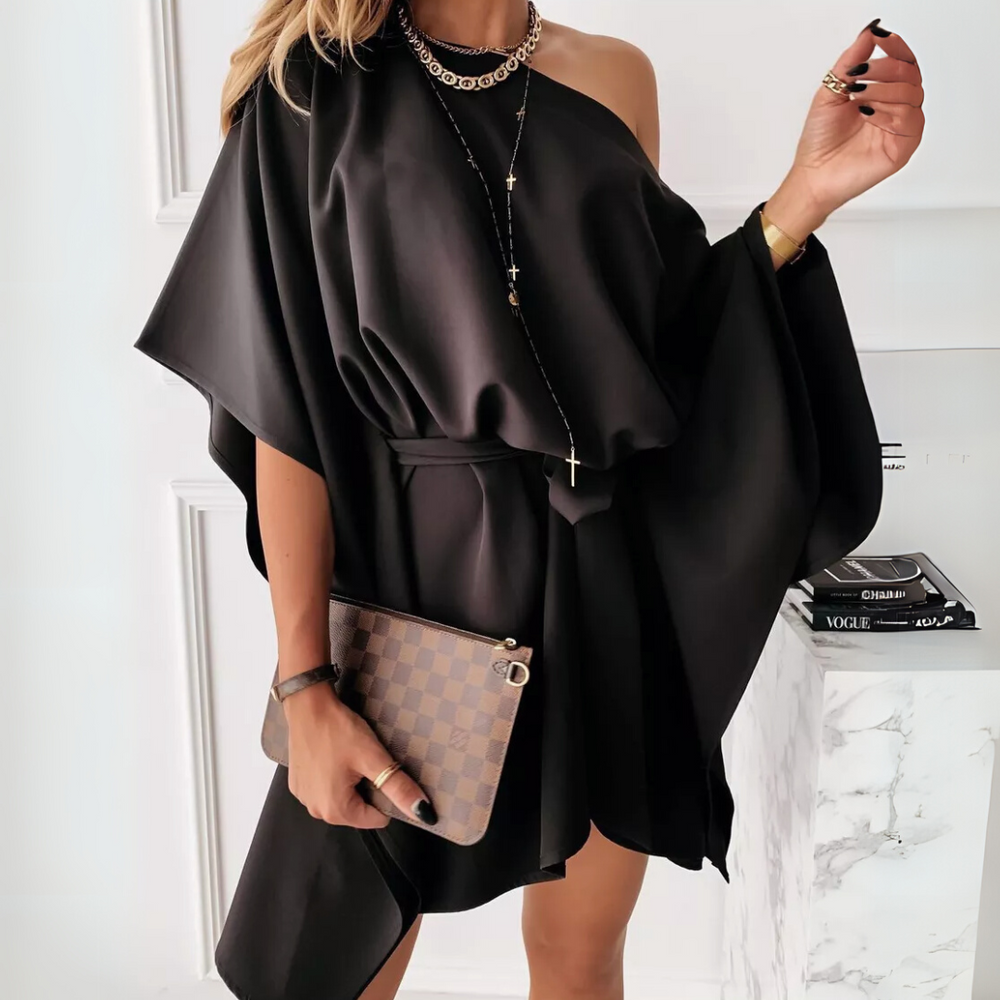 Frau in elegantem, schwarzem, schulterfreiem Kleid mit Kette und Armband, hält eine karierte Clutch. Perfektes Outfit für Abendveranstaltungen.