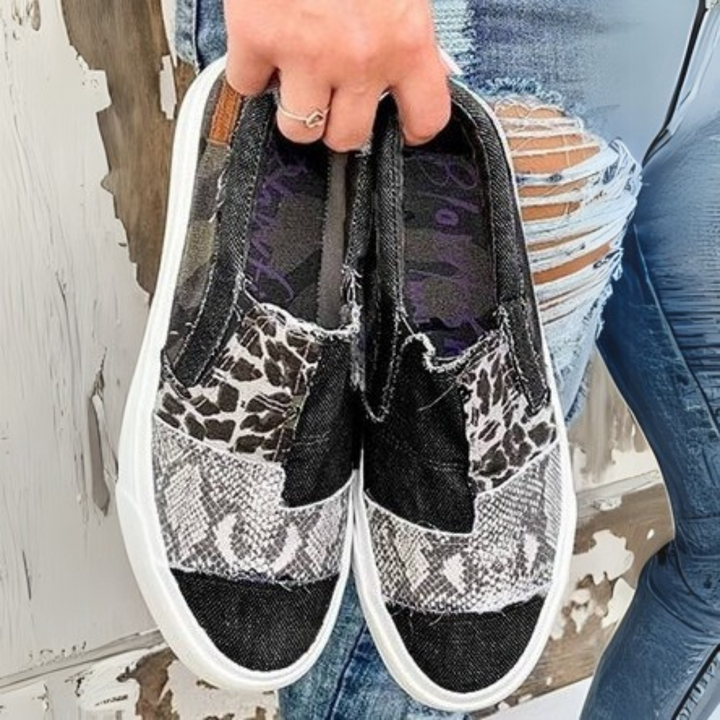 Zerrissene Jeans und modische Slip-On-Sneaker mit Leoparden- und Schlangenprint, gehalten von einer Hand. Trendige Damenmode, lässiger Stil.