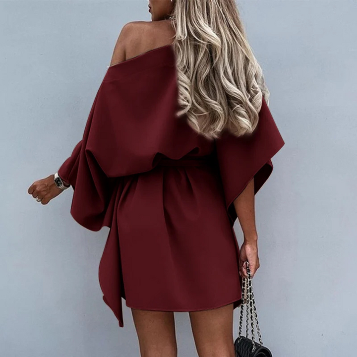 Frau in schulterfreiem, weinrotem Kleid mit langen Ärmeln, hält eine schwarze Handtasche. Elegante Mode, stilvolles Outfit, blonde Haare.