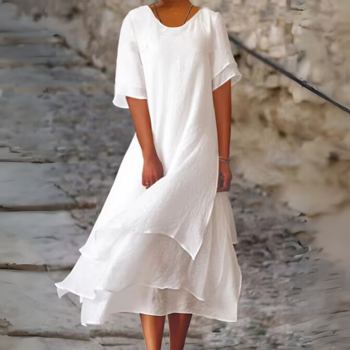 Frau in elegantem, weißem Sommerkleid auf steiniger Treppe. Luftiges Design, ideal für warme Tage. Mode, Damenbekleidung, Sommeroutfit.