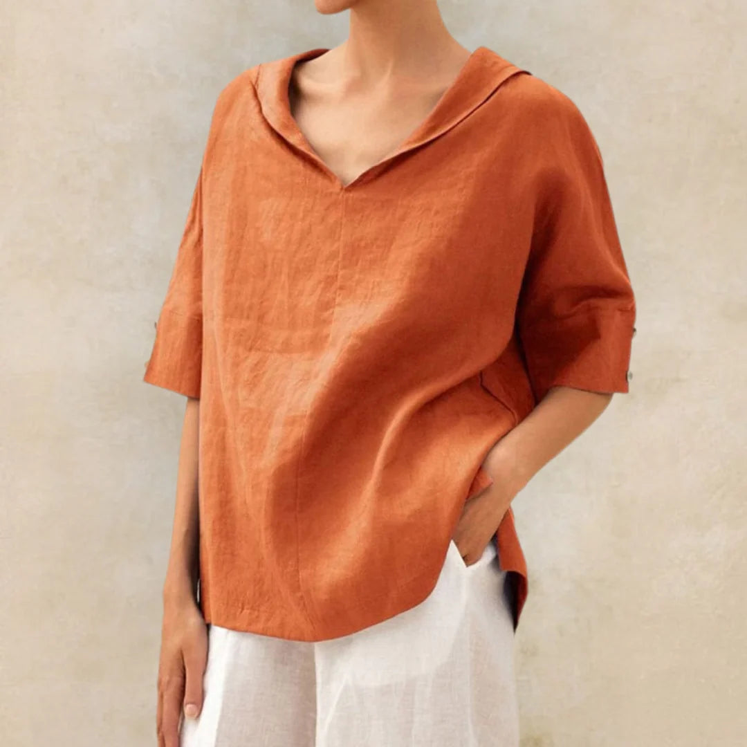 Frau trägt lockere, orangefarbene Leinenbluse mit V-Ausschnitt und halblangen Ärmeln, kombiniert mit weißen Hosen. Sommermode, lässiger Stil.