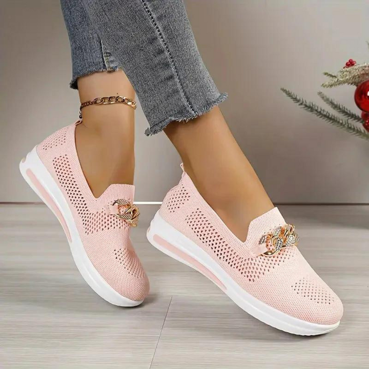 Damen rosa Sneaker mit Strassverzierung, atmungsaktivem Mesh-Obermaterial und weißer Sohle, getragen mit grauer Jeans. Modische Freizeitschuhe.