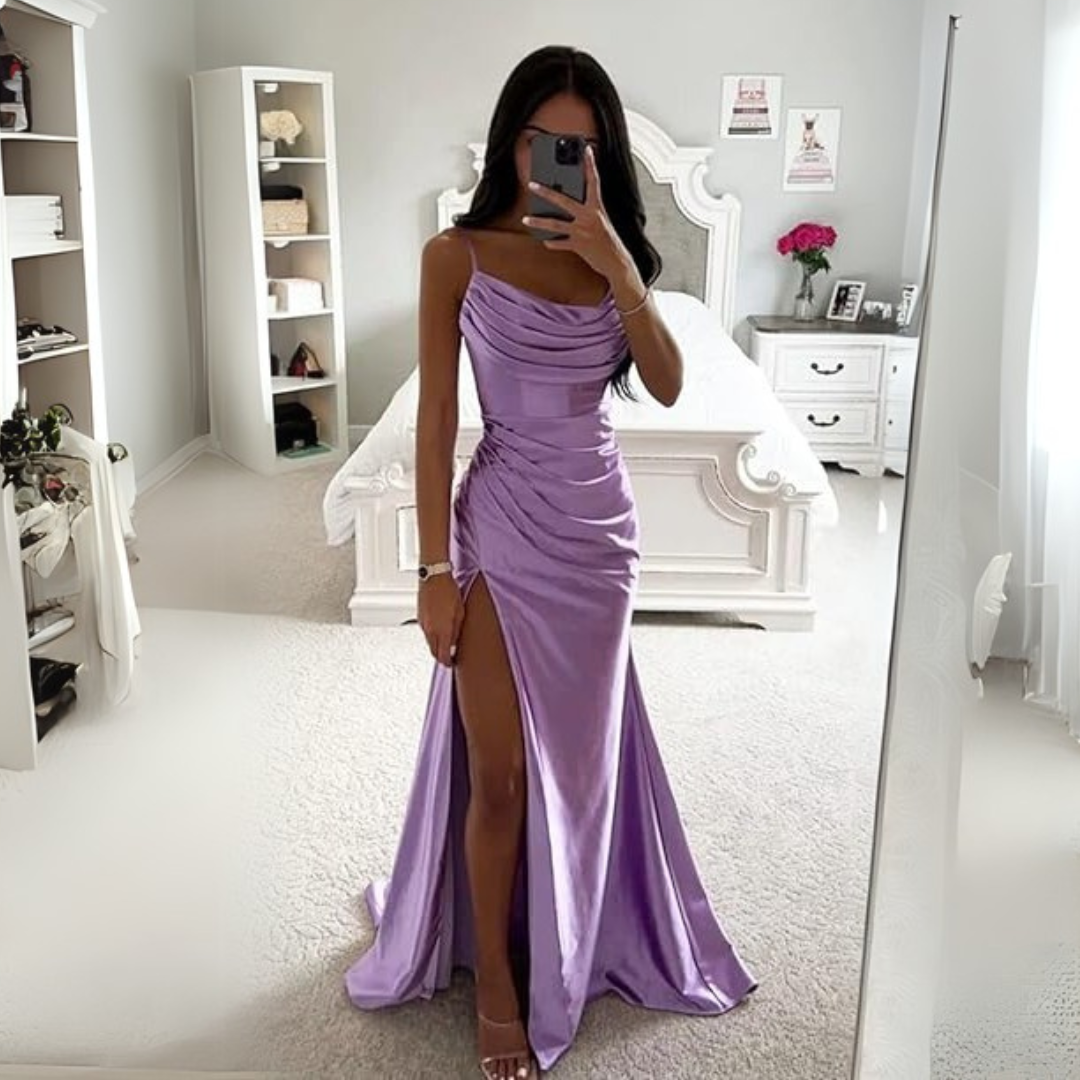 Frau in lila Abendkleid mit hohem Beinschlitz, posiert vor einem Spiegel in elegantem Schlafzimmer. Elegantes Design, Mode, Abendmode.