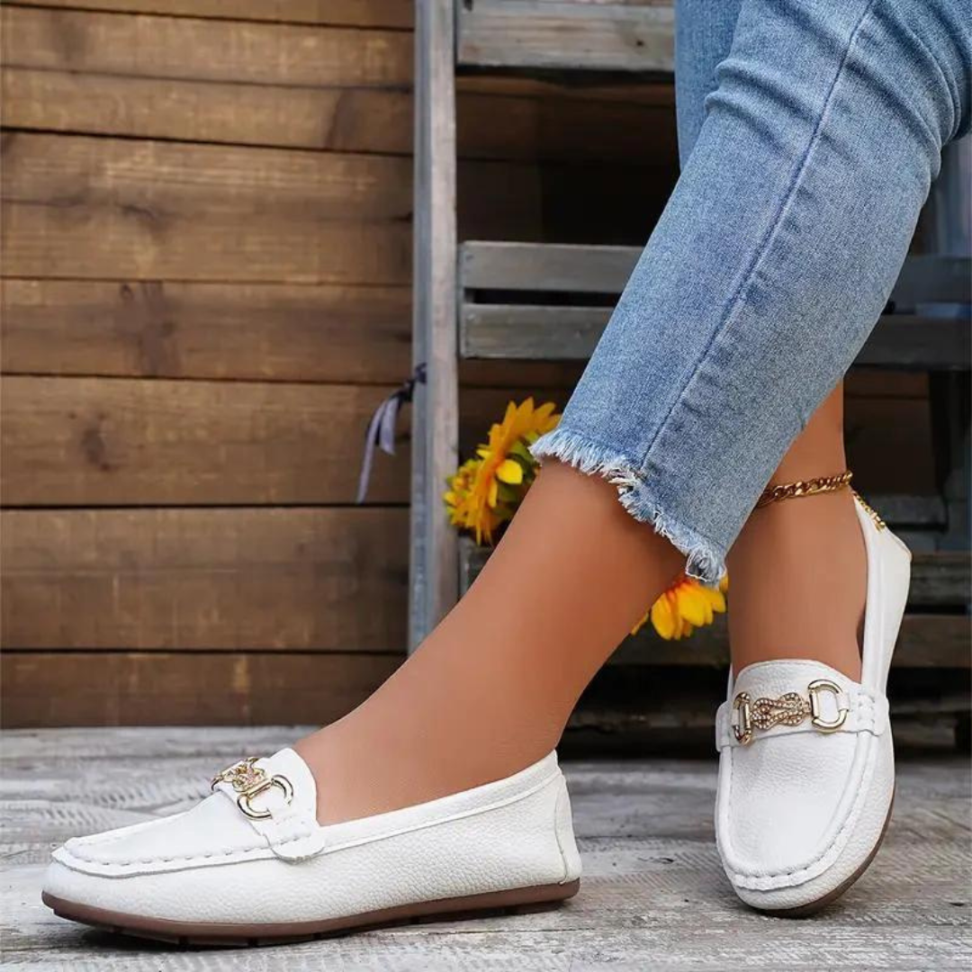 Weiße Damen-Mokassins mit goldener Schnalle, getragen mit blauen Jeans. Modische Freizeitschuhe, ideal für den Sommer. Elegante Damenmode.