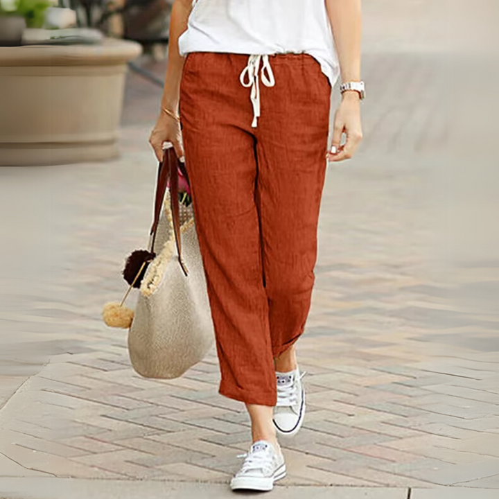 Frau in lässiger roter Leinenhose und weißen Sneakers, trägt eine beige Tasche. Sommermode, bequeme Damenbekleidung, Freizeitlook.