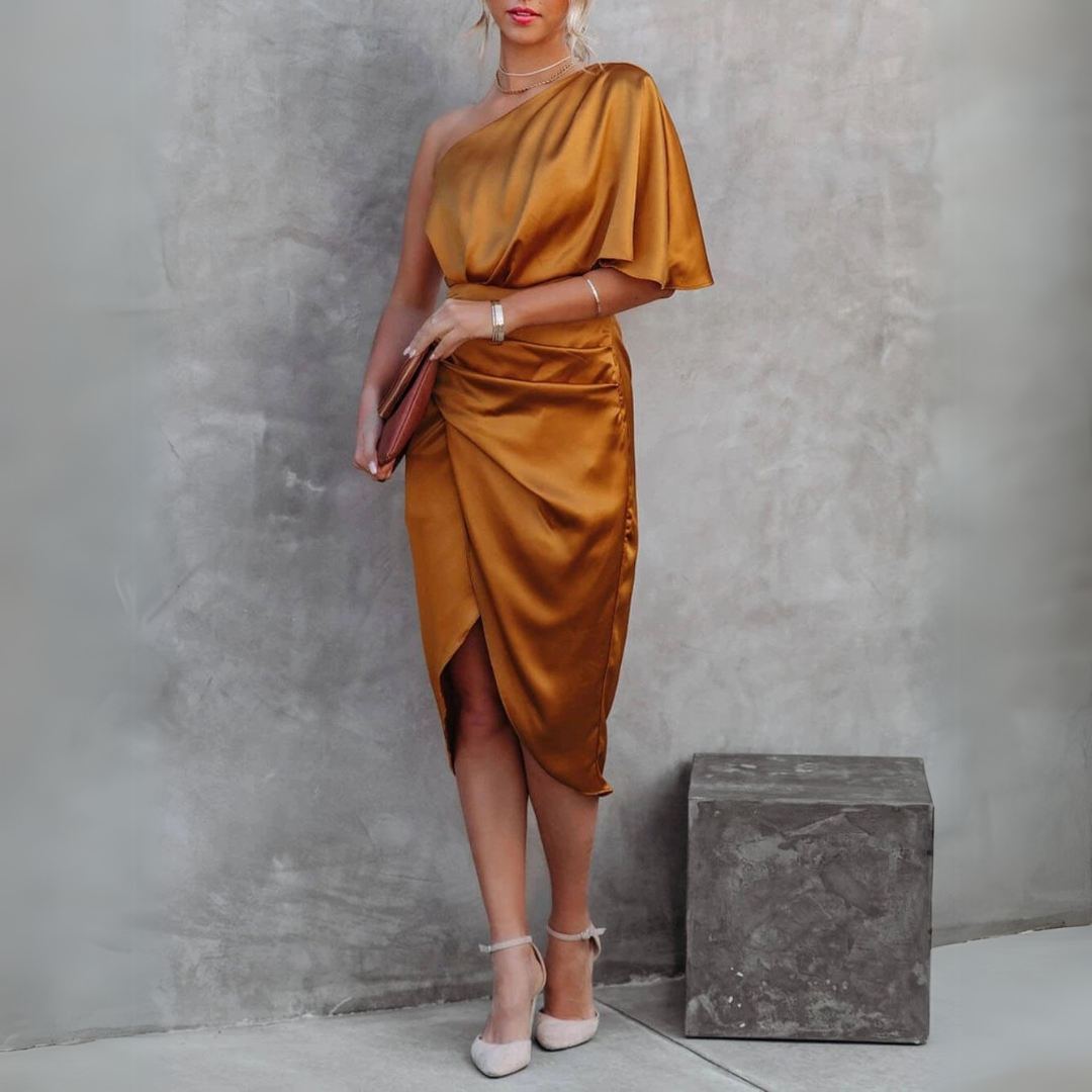 Elegantes, einseitig schulterfreies, goldenes Satinkleid, kombiniert mit weißen High Heels und einer Clutch, vor grauem Hintergrund.