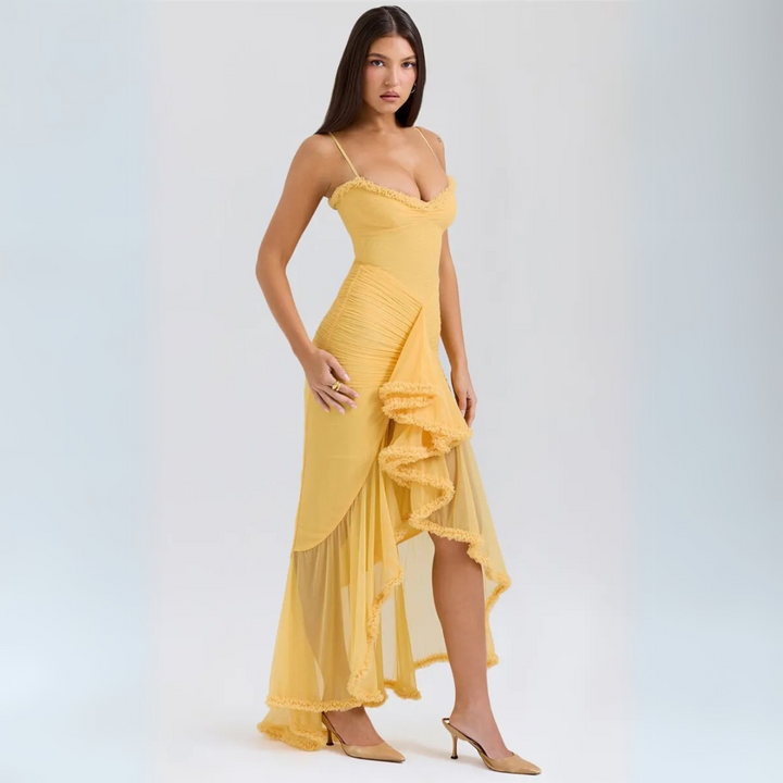 Eine Frau in einem eleganten, gelben Abendkleid mit asymmetrischem Saum und Rüschen, posiert vor einem neutralen Hintergrund.