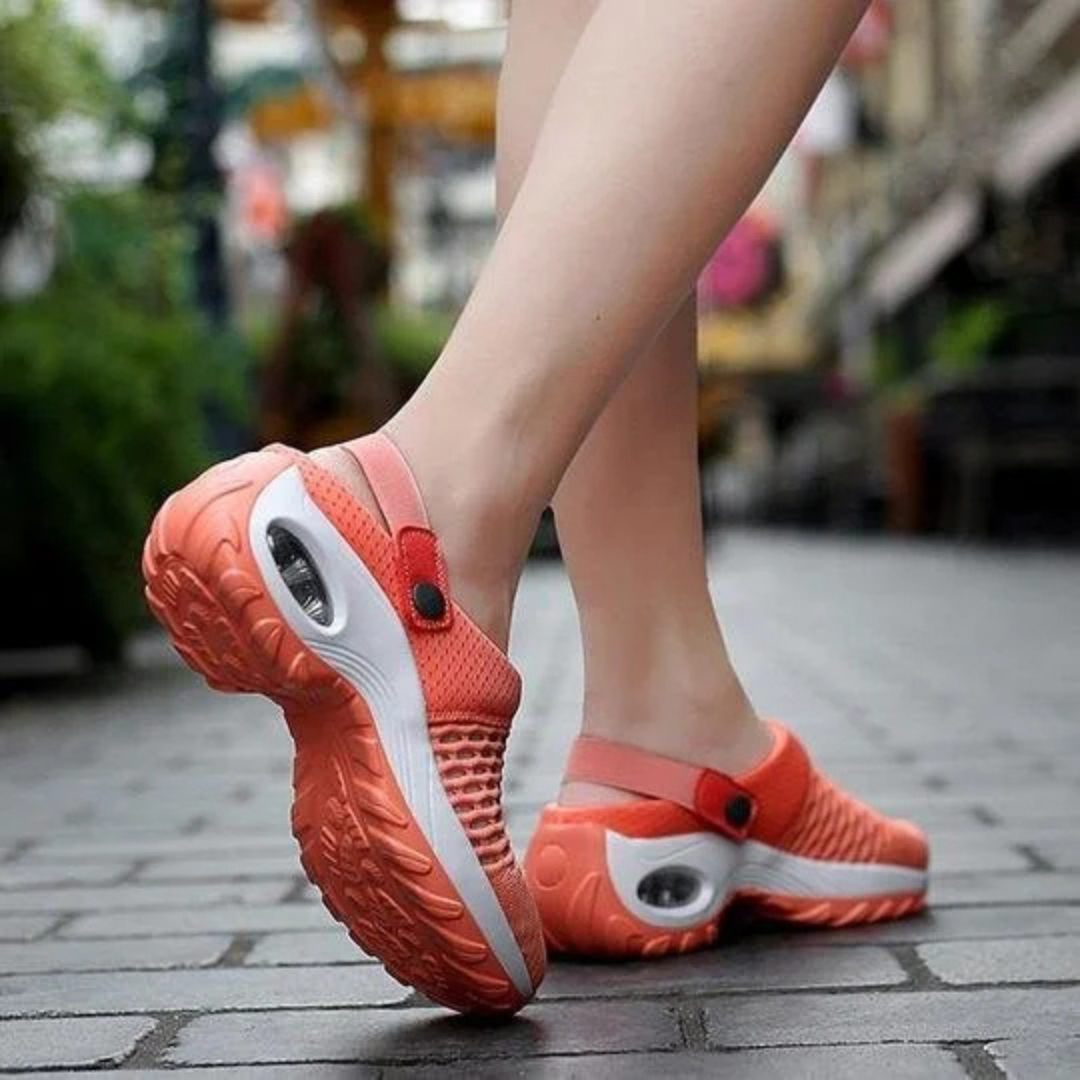 Damen tragen orangefarbene, atmungsaktive Sportschuhe mit Luftpolstersohle auf gepflastertem Gehweg. Bequeme, modische Laufschuhe für Damen.