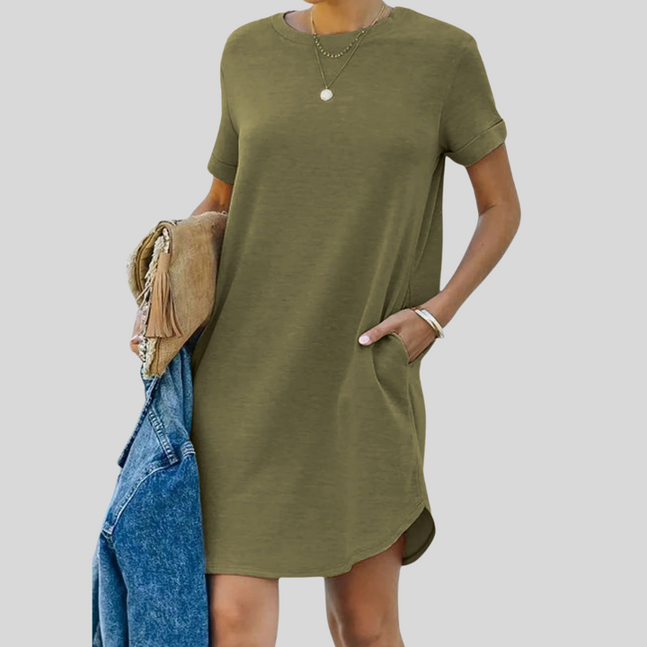 Frau in olivgrünem T-Shirt-Kleid mit Taschen, hält blaue Jeansjacke und braune Tasche. Modetrend, lässiger Stil, Sommeroutfit.