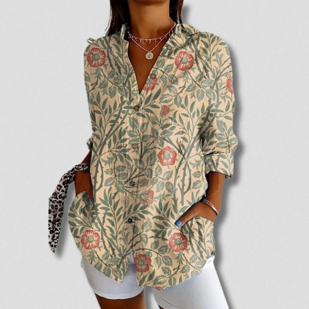 Frau trägt florale Bluse mit roten Blumen und grünen Blättern, kombiniert mit weißer Hose. Modetrend, Damenmode, stilvolle Freizeitkleidung.