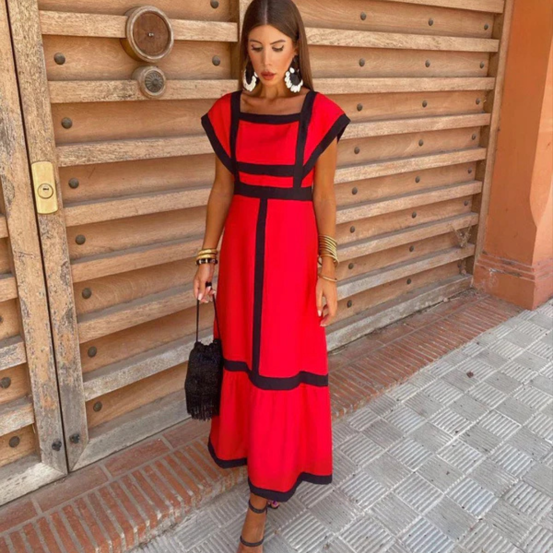 Frau in rotem Kleid mit schwarzen Akzenten, steht vor Holztür, trägt große Ohrringe und Armbänder, hält schwarze Tasche. Elegante Mode, Sommeroutfit.