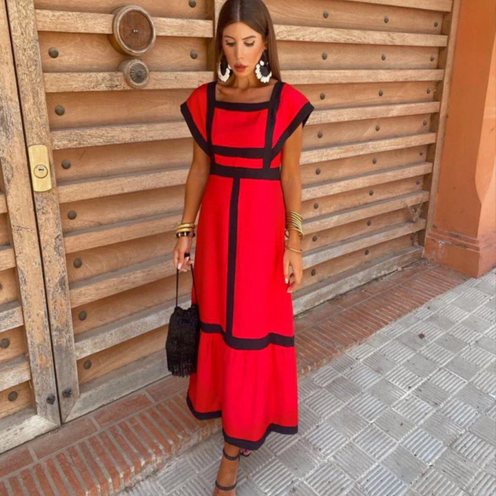 Frau in rotem Kleid mit schwarzen Akzenten, steht vor Holztür, trägt große Ohrringe und Armbänder, hält schwarze Tasche. Elegante Mode, Sommeroutfit.