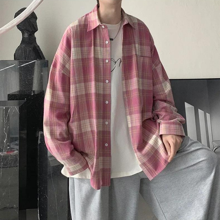 Person trägt übergroßes, kariertes Hemd in Rosa und Weiß über weißem T-Shirt, kombiniert mit grauer Jogginghose. Lässige Mode, Streetwear-Trend.