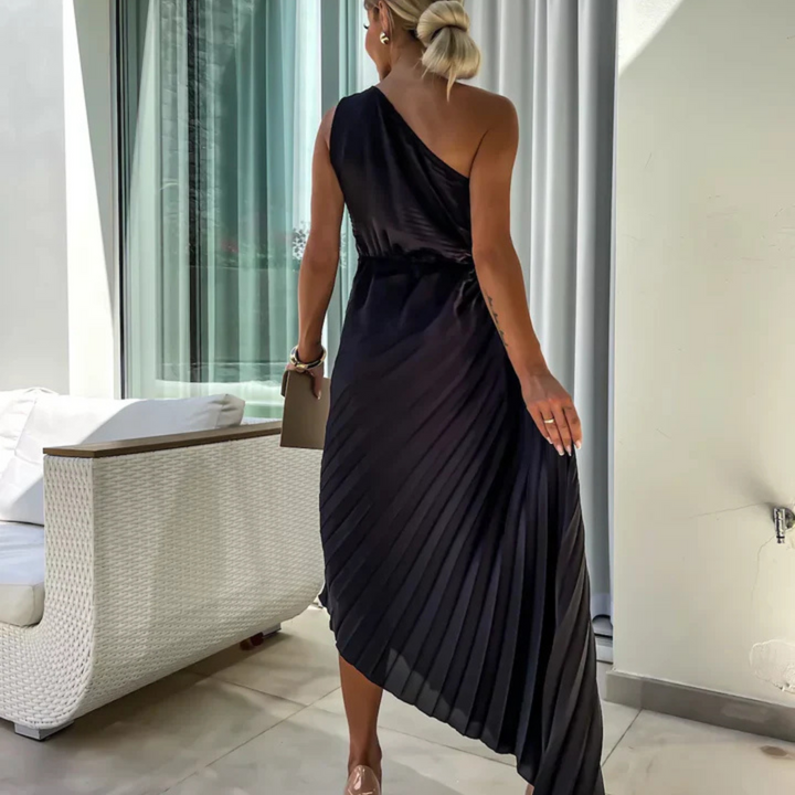 Blonde Frau in eleganter, schwarzer, einseitiger Abendkleid mit Plissee-Design, steht auf Terrasse. Luxuriöse Mode, Abendgarderobe, stilvoll.