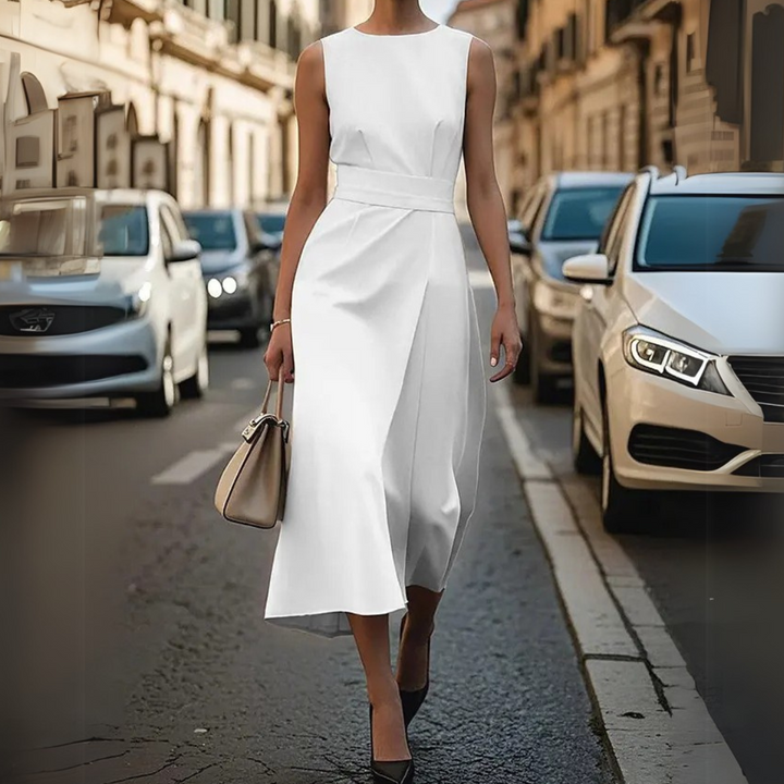 Eine Frau in einem eleganten weißen Kleid geht auf einer belebten Stadtstraße. Sie trägt eine Handtasche, umgeben von parkenden Autos.