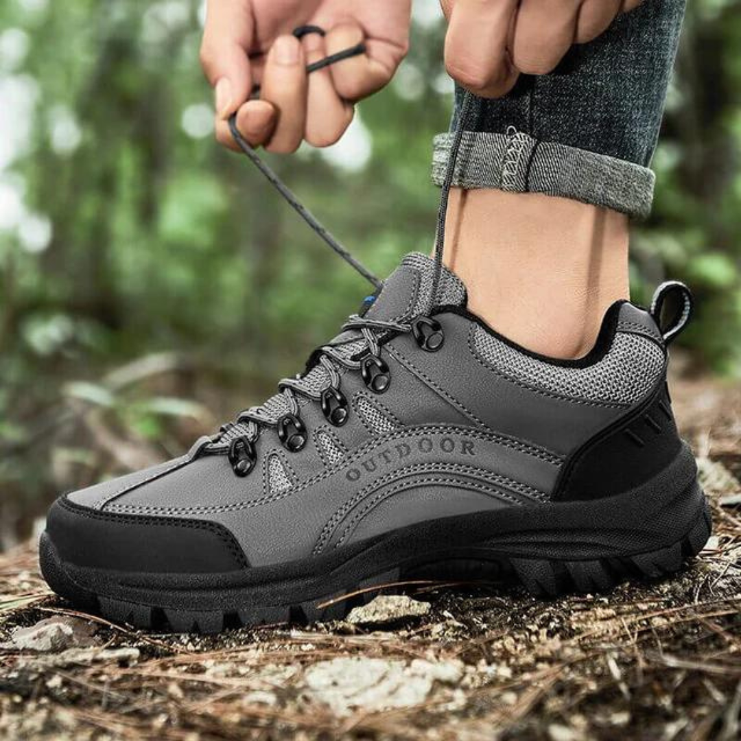 Grauer Outdoor-Wanderschuh mit robustem Profil, geschnürt auf Waldboden. Ideal für Trekking und Naturabenteuer. Hochwertige Materialien.