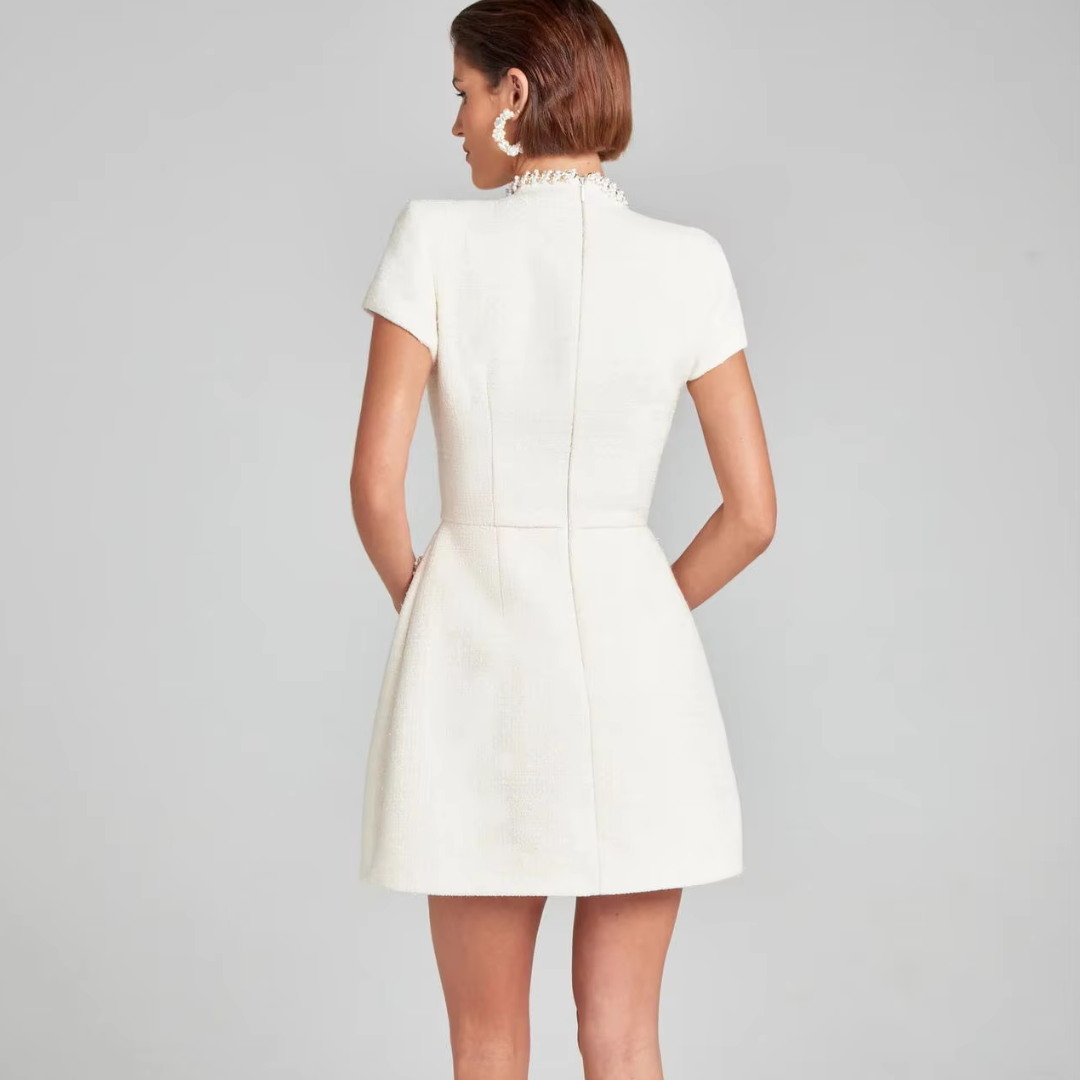 Rückansicht einer Frau in einem eleganten, weißen Minikleid mit kurzen Ärmeln und Perlenkragen, ideal für formelle Anlässe und Abendmode.