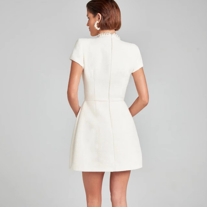 Rückansicht einer Frau in einem eleganten, weißen Minikleid mit kurzen Ärmeln und Perlenkragen, ideal für formelle Anlässe und Abendmode.