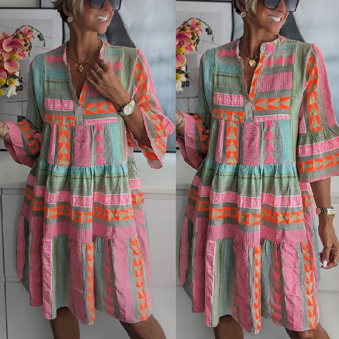 Frau in buntem, geometrisch gemustertem Kleid mit langen Ärmeln, lächelt und trägt Sonnenbrille. Sommermode, Boho-Stil, Freizeitkleidung.