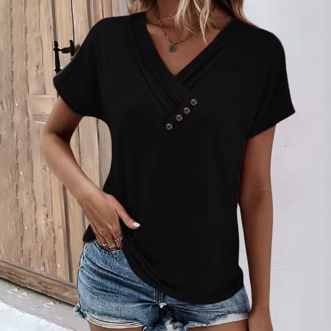 Frau in schwarzem V-Ausschnitt-T-Shirt mit Knöpfen, kombiniert mit blauen Jeansshorts, steht vor Holztür. Modetrend, Sommeroutfit, Freizeitkleidung.