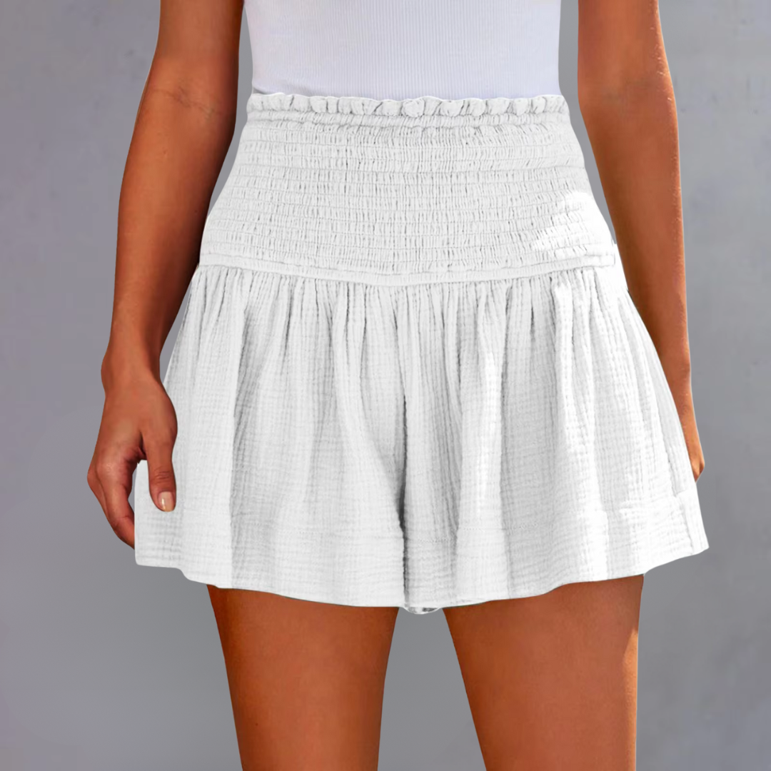 Weiße, hoch taillierte Damen-Shorts mit Rüschen und elastischem Bund, getragen von einer Frau vor grauem Hintergrund. Sommermode, bequeme Passform.