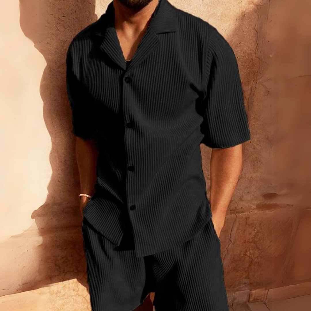 Mann in schwarzem, geripptem Kurzarmhemd und Shorts vor beiger Wand. Sommermode, Herrenbekleidung, lässiger Stil.