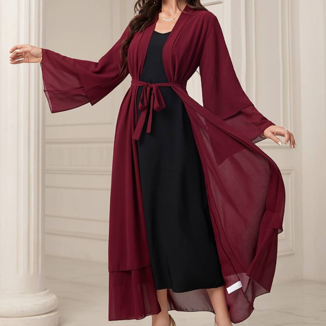 Frau in eleganter, burgunderroter Chiffon-Cardigan mit Gürtel über schwarzem Kleid, stehend in stilvollem, klassischem Innenraum.
